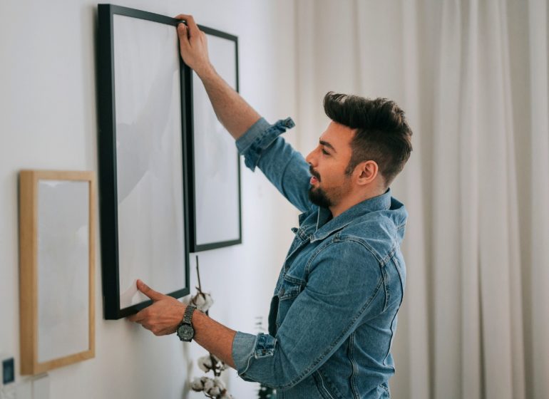 Hombre joven colgando cuadro en living